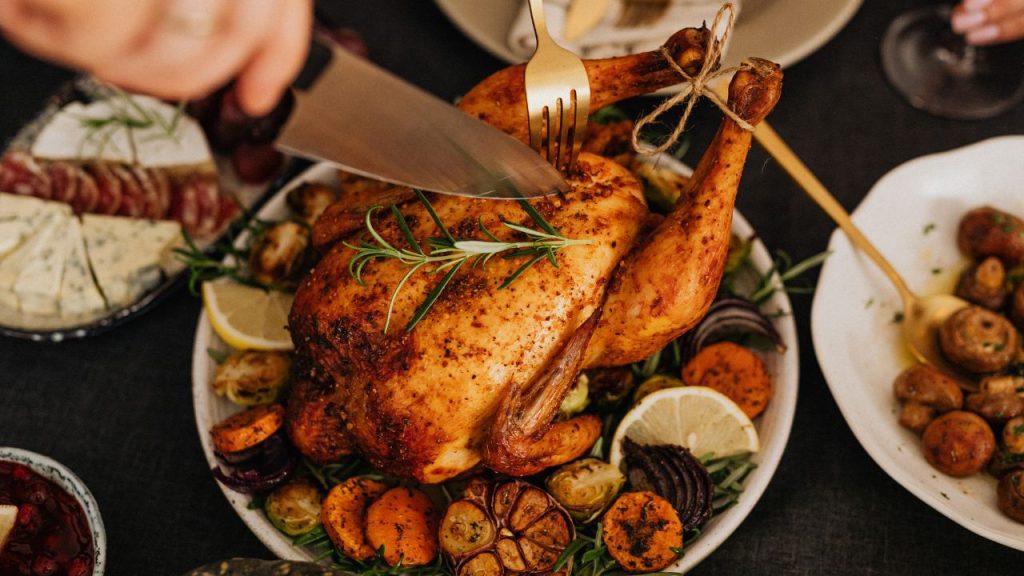 Pessoa usa faca para cortar frango assado com legumes, uma das mais populares receitas com frango